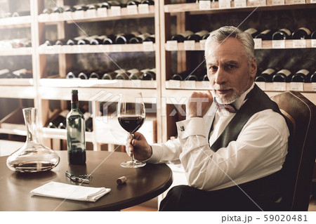 Sommelier Concept. Senior man sitting at table with glass of wine looking camera curious 59020481