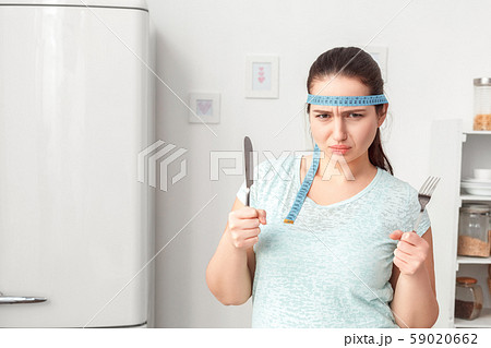 Be on Diet. Chubby girl with tape measure around head standing in kitchen with fork and knife Be on Diet. Chubby girl with tape measure around head standing in kitchen with fork and knife 59020662
