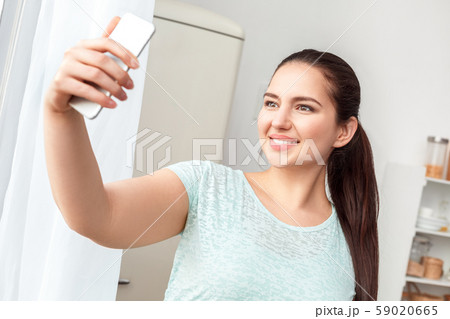 Body Care. Chubby girl standing in kitchen taking selfie on smartphone smiling cheerful to camera 59020665