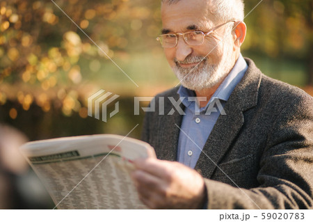 Senior man read a newspaper in the park. Background of yellow tree in autumn 59020783