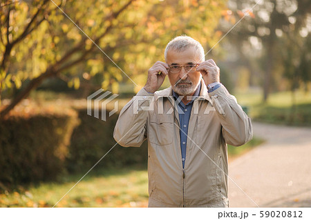 Handsome bearder elderly man put on glasses. Gray haired old man in the park Handsome bearder elderly man put on glasses. Gray haired old man in the park 59020812