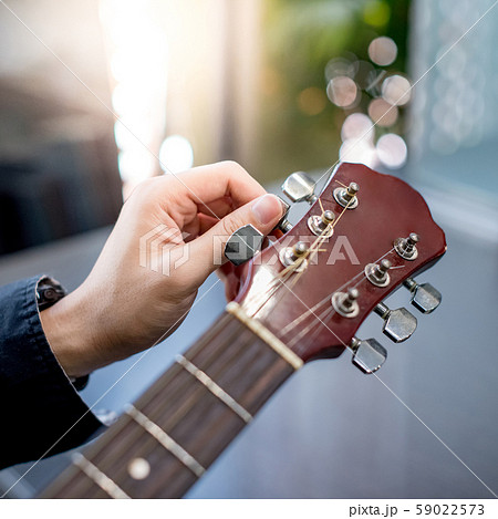 Male hand adjusting pegs on acoustic guitar 59022573