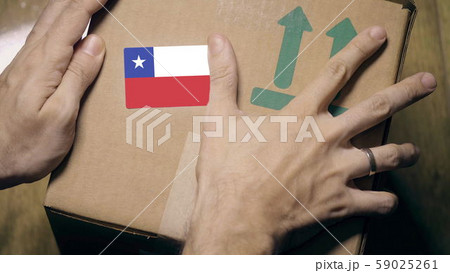 Warehouse worker places sticker with flag of Chile on the box. Chilean import or export 59025261