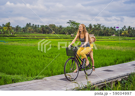 Mother and son ride a bicycle on a rice field in Ubud, Bali. Travel to Bali with kids concept Mother and son ride a bicycle on a rice field in Ubud, Bali. Travel to Bali with kids concept 59034997