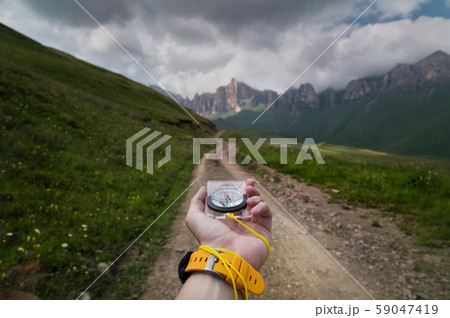 Close-up wide angle male hand with a yellow watch bracelet holds a magnetic navigation compass Close-up wide angle male hand with a yellow watch bracelet holds a magnetic navigation compass 59047419