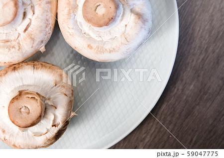 Close-up of white mushrooms on a white plate on a dark wooden table. Vegetarian healthy food Close-up of white mushrooms on a white plate on a dark wooden table. Vegetarian healthy food 59047775