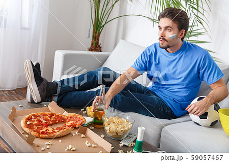 Young man sport fan watching match in a blue t-shirt drinking beer Young man sport fan watching match in a blue t-shirt drinking beer 59057467
