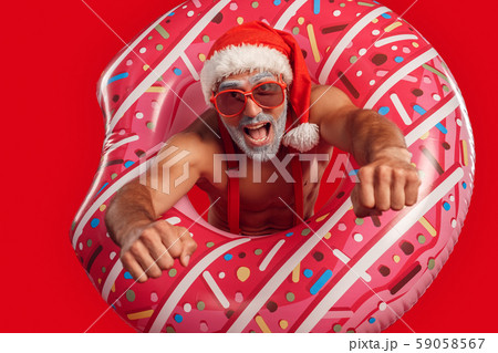 Christmas Freestyle. Young Santa Claus bare muscular upper body in hat and sunglasses standing Christmas Freestyle. Young Santa Claus bare muscular upper body in hat and sunglasses standing 59058567