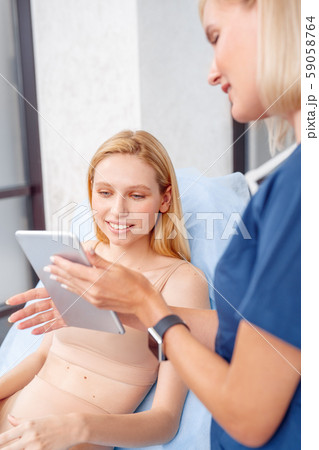 Cosmetology Service. Young woman at beauty clinic sitting looking at digital tablet cheerful doctor 59058764
