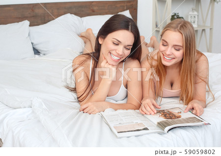 Friends together at home lying on bed reading magazine happy Friends together at home lying on bed reading magazine happy 59059802