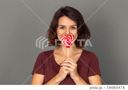 Freestyle. Young woman isolated on grey covering mouth with lollipop smiling playful close-up Freestyle. Young woman isolated on grey covering mouth with lollipop smiling playful close-up 59060478