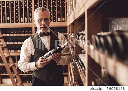 Sommelier Concept. Senior man standing with wine bottle looking camera concerned Sommelier Concept. Senior man standing with wine bottle looking camera concerned 59068148