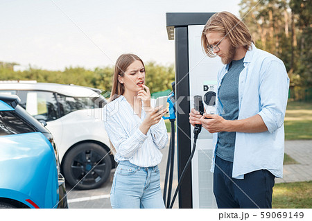 Young adult friends trying charge electric car Young adult friends trying charge electric car 59069149