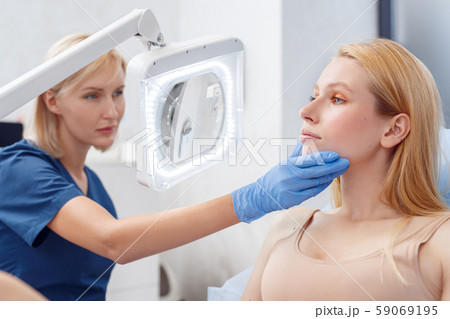 Cosmetology Service. Young woman at beauty clinic sitting while doctor holding her face examining Cosmetology Service. Young woman at beauty clinic sitting while doctor holding her face examining 59069195