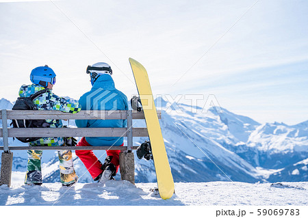 Photo from back of athletes sitting on bench next to snowboard in ski resort Photo from back of athletes sitting on bench next to snowboard in ski resort 59069783