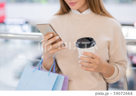 Young woman with paperbags and glass of coffee scrolling through online goods Young woman with paperbags and glass of coffee scrolling through online goods 59072668