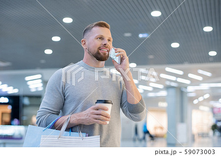 Young man with smartphone, drink and paperbags calling online shop Young man with smartphone, drink and paperbags calling online shop 59073003