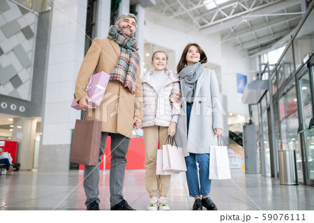 Young cheerful family of three in coats carrying paperbags Young cheerful family of three in coats carrying paperbags 59076111