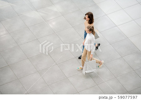 Contemporary shopaholics carrying bags while moving down large trade center 59077597
