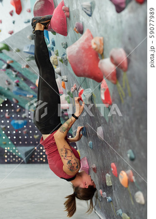 Young skilled sportswoman hanging upside down along climbing wall 59077989