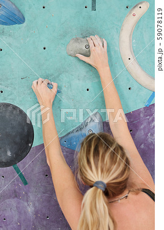 Back view of young blonde female climber grabbing small artificial rocks Back view of young blonde female climber grabbing small artificial rocks 59078119