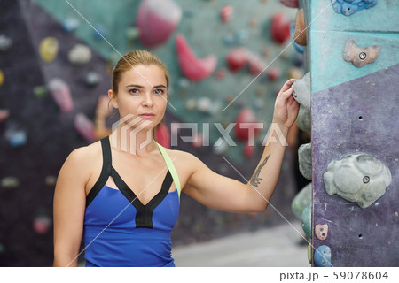 Pretty sportswoman in activewear standing by climbing wall in gym 59078604