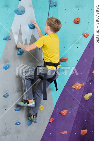 Side view of youthful boy in activewear climbing wall while grabbing by rocks 59078991