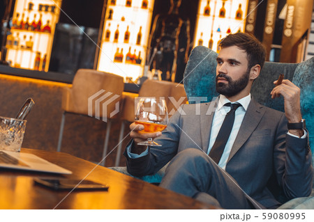 Businessman sitting in a business center bar drinking whiskey and smoking Businessman sitting in a business center bar drinking whiskey and smoking 59080995