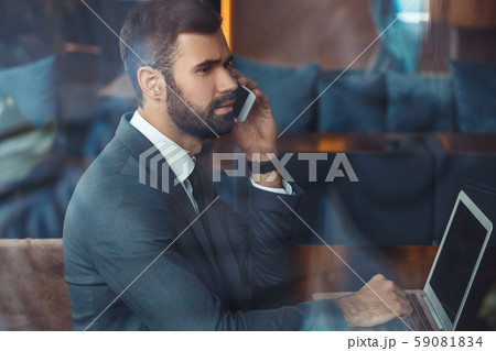 Businessman sitting in a business center restaurant with laptop phone call Businessman sitting in a business center restaurant with laptop phone call 59081834