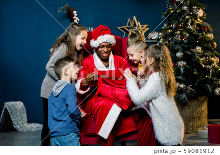 Five children look into the bag of African Santa Claus and laughing, African Santa Claus is seated Five children look into the bag of African Santa Claus and laughing, African Santa Claus is seated 59081912
