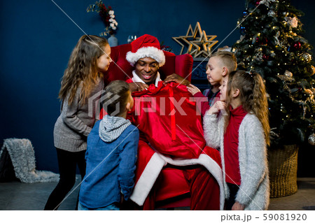 African Santa Claus is seated and gives presents to beautiful little children in a christmas 59081920