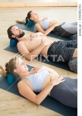 Restorative yoga with a bolster. Group of young sporty attractive people in yoga studio, lying on 59086291