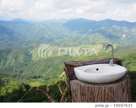 white ceramics wash basin with stainless steel faucet on natural wood log on mountain top with real luxury tropical hills and mountain view  59097635
