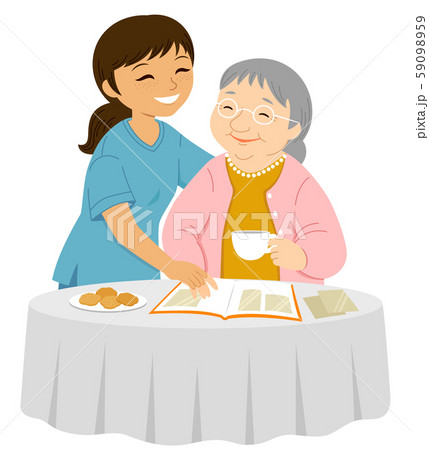 Young female caregiver smiling to an elderly woman who is placing photos in an album 59098959