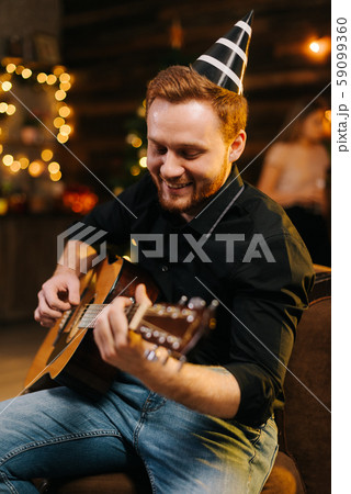 Portrait of young cheerful man in the festive hat playing on the guitar. Portrait of young cheerful man in the festive hat playing on the guitar. 59099360