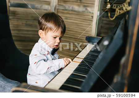 A little boy in a smart shirt and bow tie sits at a large tuning piano 59100594