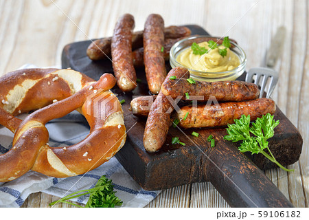 Fried Bavarian sausages from Nuremberg with mustard and pretzel served on a rustic steak board 59106182