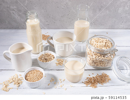 Set of different containers with healthy dairy free oat milk, oat seeds and flakes on white wooden table on grey concrete background. Lactose free substitutes of milk concept. Set of different containers with healthy dairy free oat milk, oat seeds and flakes on white wooden table on grey concrete background. Lactose free substitutes of milk concept. 59114535