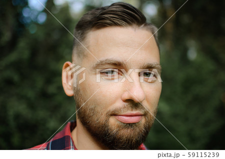 Close up portrait of young bearded man in red shirt looking at the camera with smile in the park on 59115239