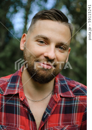Close up portrait of young bearded man in red shirt looking at the camera with smile in the park on 59115241