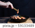 Chef at work. Hand holds a chopsticks under hot pan with fried vegetables, broccoli, cauliflower, carrots and shrimp. Process of preparation of vegetables over dark background 59133489