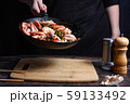 Chef at work. Hand holds a hot pan with fried shrimp and vegetables in sweet and sour sauce. Process of preparation of shrimps over dark background 59133492