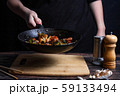 Chef at work. Hand holds a hot pan with fried vegetables, broccoli, cauliflower, carrots. Process of preparation of vegetables over dark background 59133494