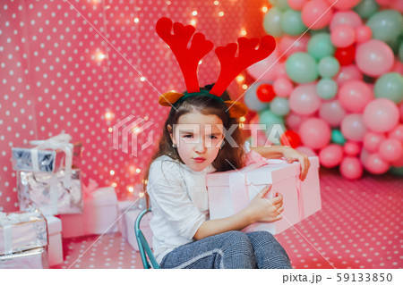 Child, present and sledge on the pink celebration background. Greedy child is frowning, keeping box 59133850