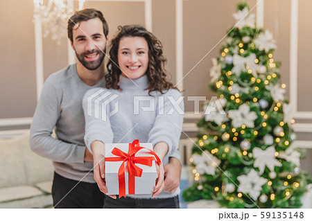 Defocused man and woman holding a present tied with a red ribbon, looking at the camera smilling. Defocused man and woman holding a present tied with a red ribbon, looking at the camera smilling. 59135148