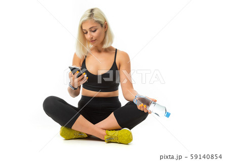 Beauiful sport caucasian girl sits on floor, cross legs, keeps a mobile phone and bottle of water 59140854