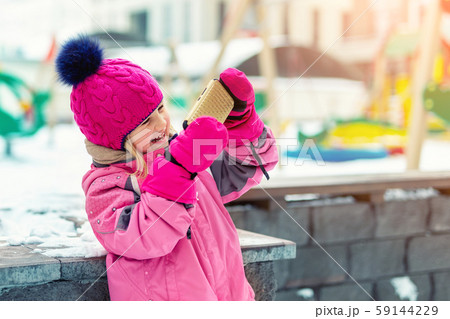 Cute blond kid girl holding smartphone and streaming for social networks winter fun activities at 59144229