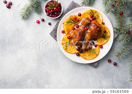 Baked chicken drumstick with oranges and cranberries in a plate light grey background. Christmas food Table with decorations. Copy space. 59163569