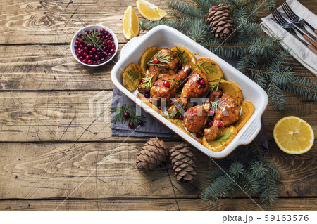 Baked chicken drumstick with oranges and cranberries in a baking sheet on a wooden background. Christmas food Table with decorations. 59163576