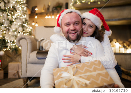 Picture of man and woman in Santa's caps sitting on floor with gifts. 59165730